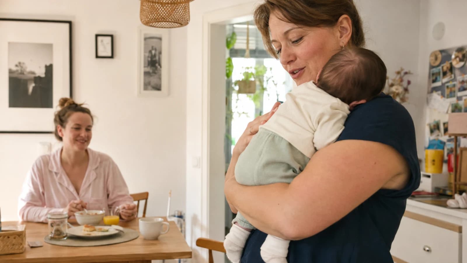 Eine Mutter beim Essen, während eine Fachkraft ihr Baby hält